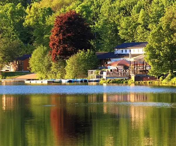Auf dem Bild ist ein See mit Booten am Anleger und einem Gebäude am Ufer zu sehen