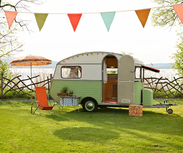 Campingplatz in Mecklemburg-Vorpommern. Kleiner Wohnwagen auf einer grünen Wiese und Sonnenschirm an einem See